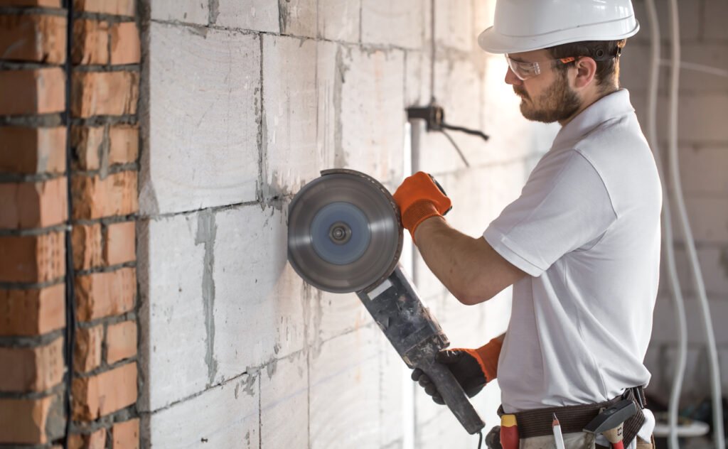 The industrial Builder works with a professional angle grinder to cut bricks and build interior walls. Electrician.